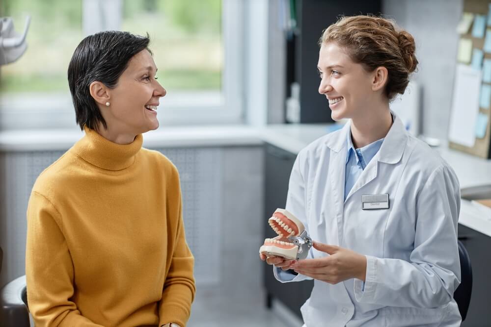 Side view portrait of smiling female dentist holding tooth model